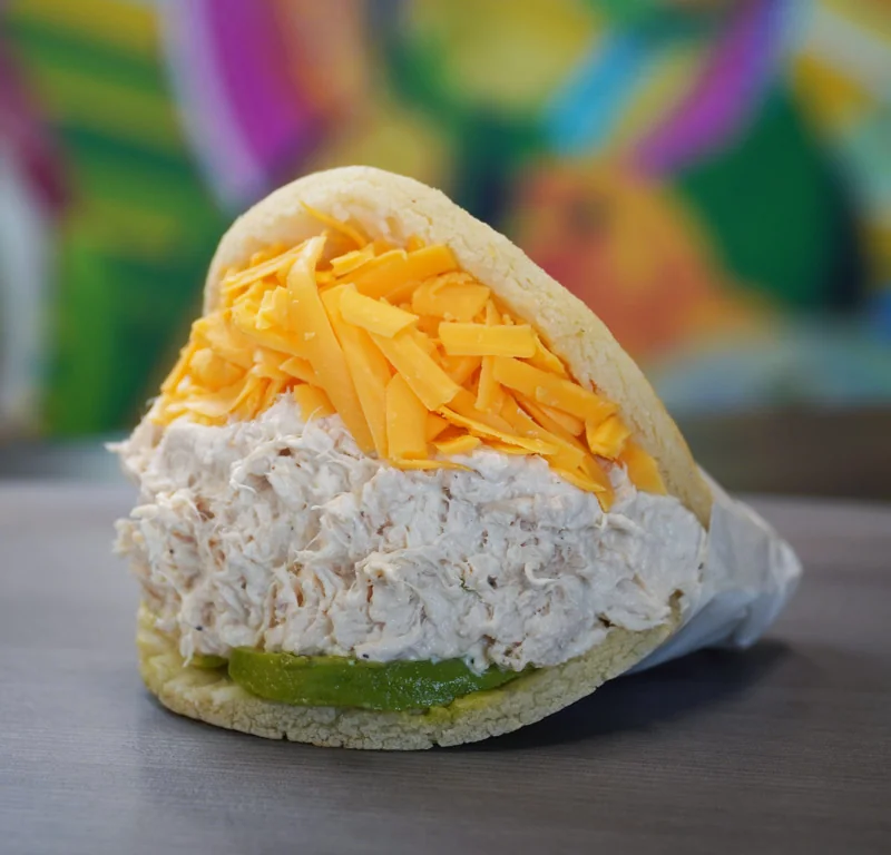 A filled arepa topped with shredded cheese